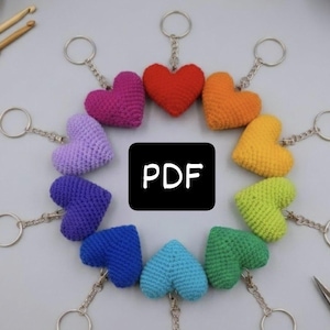 May include: A circular arrangement of ten crocheted heart keychains in various colors including red, orange, yellow, lime green, green, light blue, dark blue, purple, lavender, and magenta, each with a silver metal ring and the text PDF in the center.