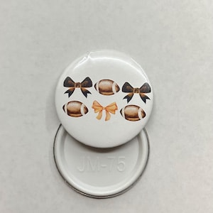 May include: White round button featuring a design of brown footballs and black bows. The button has the text "JM-75" on the back.