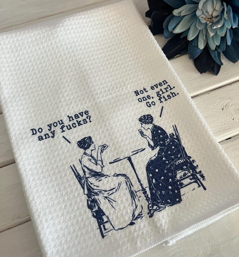 May include: White waffle-weave kitchen towel with a blue illustration of two women and text. One woman asks, "Do you have any fucks?" The other replies, "Not even one, girl. Go fish."