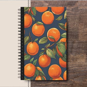 Può includere: Un quaderno a spirale con una copertina blu scuro che presenta un motivo ripetitivo di frutta arancione e foglie verdi.