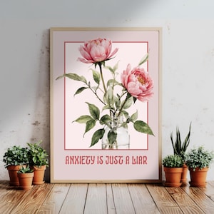Könnte beinhalten: Ein gerahmter Druck mit einer Aquarellillustration von rosa Pfingstrosen in einer Glasvase. Das Kunstwerk enthält den Text "ANXIETY IS JUST A LIAR" in rosa Schrift. Kleine Topfpflanzen sind vor dem Rahmen angeordnet.