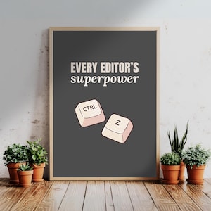 Puede incluir: Póster enmarcado con el texto "EVERY EDITOR'S superpower" en blanco. Debajo del texto hay ilustraciones de las teclas CTRL y Z. El póster se muestra sobre una superficie de madera con plantas en macetas.
