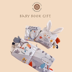 May include: Soft baby book gift set featuring animal-themed illustrations. The books include a jungle animal book with an elephant, a farm tails book with a bunny, and a crocodile and toucan book. The text "Baby Book Gift" is displayed.