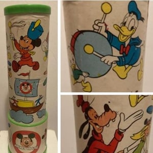 May include: A vintage kaleidoscope featuring a colorful design with Mickey Mouse, Donald Duck, and Goofy. The kaleidoscope is made of cardboard and has a green plastic top. The kaleidoscope is approximately 10 inches tall.