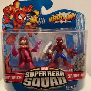 May include: A Marvel Super Hero Squad toy set featuring Scarlet Witch and Spider-Man action figures. The figures are in a clear plastic package with the words "HERO UP!" and "SUPER HERO SQUAD" printed on the packaging. The toy set is for ages 3+.