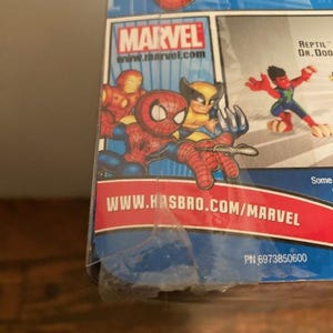 May include: A Marvel-branded product package featuring cartoon illustrations of Spider-Man, Iron Man, and Wolverine. The Marvel logo and website address are visible. The background is blue with red and white accents.