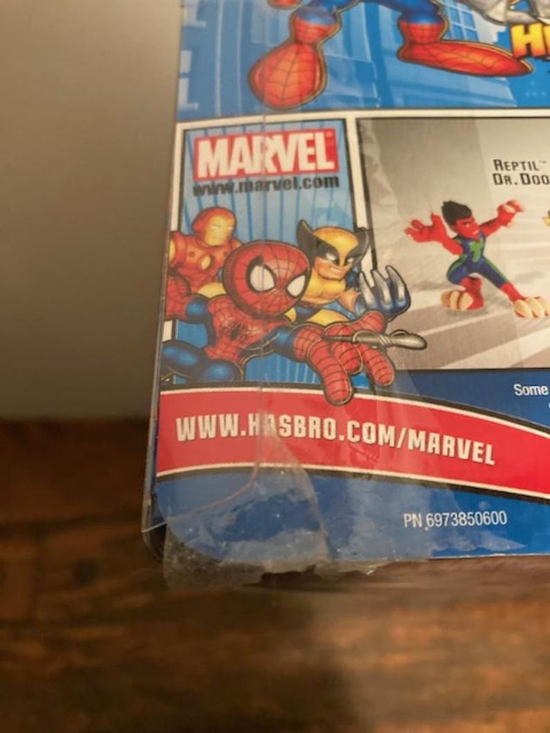 May include: A Marvel-branded product package featuring cartoon illustrations of Spider-Man, Iron Man, and Wolverine. The Marvel logo and website address are visible. The background is blue with red and white accents.