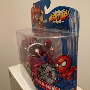 May include: A Spider-Man action figure in a clear plastic package. The packaging features a cartoon Spider-Man graphic and the words "HERO UP!" and "Spider-Man". The figure is red and blue, and the packaging is blue and red.