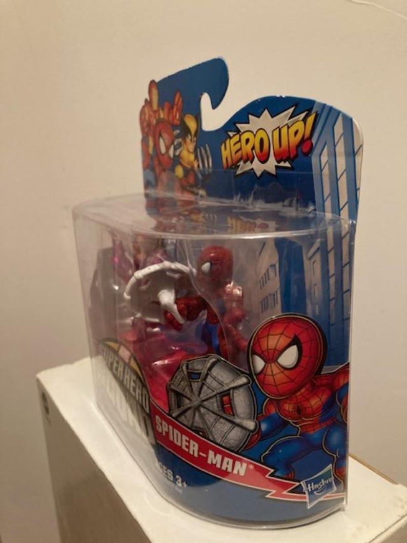 May include: A Spider-Man action figure in a clear plastic package. The packaging features a cartoon Spider-Man graphic and the words "HERO UP!" and "Spider-Man". The figure is red and blue, and the packaging is blue and red.