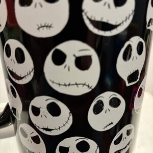 Puede incluir: Taza de caf&eacute; negra con caras blancas ovaladas con sonrisas cosidas y diversas expresiones. El dise&ntilde;o de la taza est&aacute; inspirado en una popular pel&iacute;cula de animaci&oacute;n, con un patr&oacute;n repetido de la cara del personaje.