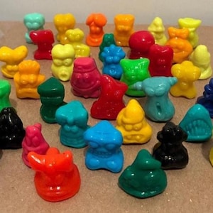 以下が含まれることがあります： 赤、黄、青、緑、黒など、さまざまな形と色のカラフルな小さなプラスチック製のフィギュアのコレクション。 フィギュアは茶色の表面に配置され、さまざまなデザインが示されています。