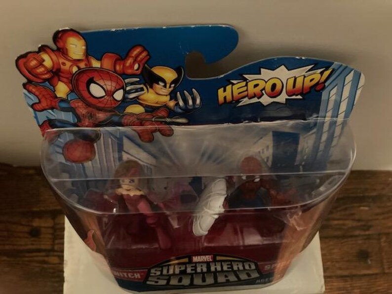 May include: Marvel Super Hero Squad action figures in a plastic package. The packaging features Iron Man, Spider-Man, and Wolverine. The package reads "HERO UP!" and "Marvel Super Hero Squad". The figures inside are visible.