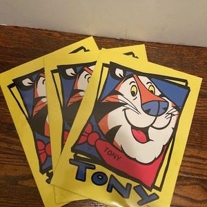 May include: Three yellow folders with a cartoon tiger wearing a red bow tie and the word "TONY" in blue and black letters. The folders are stacked on top of each other.
