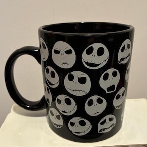 Puede incluir: Taza de cer&aacute;mica negra con m&uacute;ltiples caras blancas de Jack Skellington de Pesadilla antes de Navidad. La taza tiene un asa negra y es adecuada para bebidas fr&iacute;as o calientes.