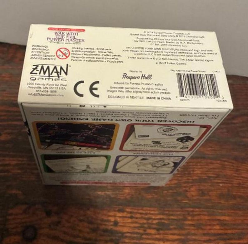 K&ouml;nnte beinhalten: Eine wei&szlig;e Pappschachtel f&uuml;r das Brettspiel "War With The Evil Power Master". Die Schachtel enth&auml;lt Text in mehreren Sprachen, das Z-Man Games-Logo und einen Barcode. Die Schachtel steht auf einer Holzoberfl&auml;che.