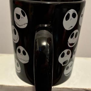 Puede incluir: Taza de cer&aacute;mica negra con caras blancas de Jack Skellington. La taza tiene un asa negra y un acabado brillante. El dise&ntilde;o se repite alrededor de la taza, creando una est&eacute;tica espeluznante y divertida.