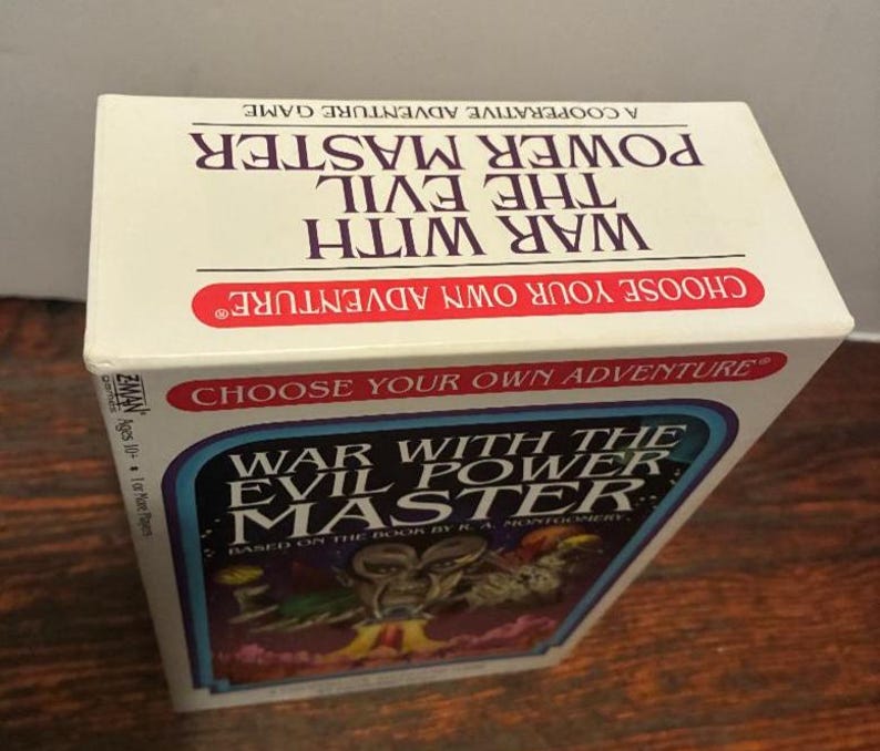 K&ouml;nnte beinhalten: Ein Brettspielkarton mit dem Titel "War With The Evil Power Master". Die Box ist wei&szlig; mit roten und blauen Akzenten. Der Titel des Spiels ist deutlich sichtbar, zusammen mit dem Satz "Choose Your Own Adventure". Die Box steht auf einer Holzoberfl&auml;che.