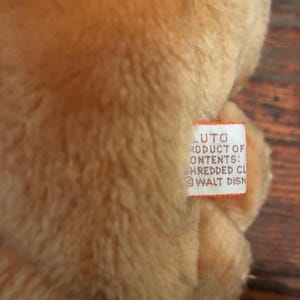 May include: Close-up of a plush toy with a soft, textured, light brown fur. A small white tag is visible, with the text "LUTO PRODUCT OF CONTENTS: HREDDED CL @ WALT DISN".