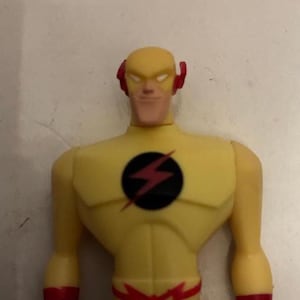 May include: A yellow action figure of a superhero with a lightning bolt emblem on the chest. The figure has red accents on the head and arms. The superhero's costume is yellow with a black lightning bolt symbol.