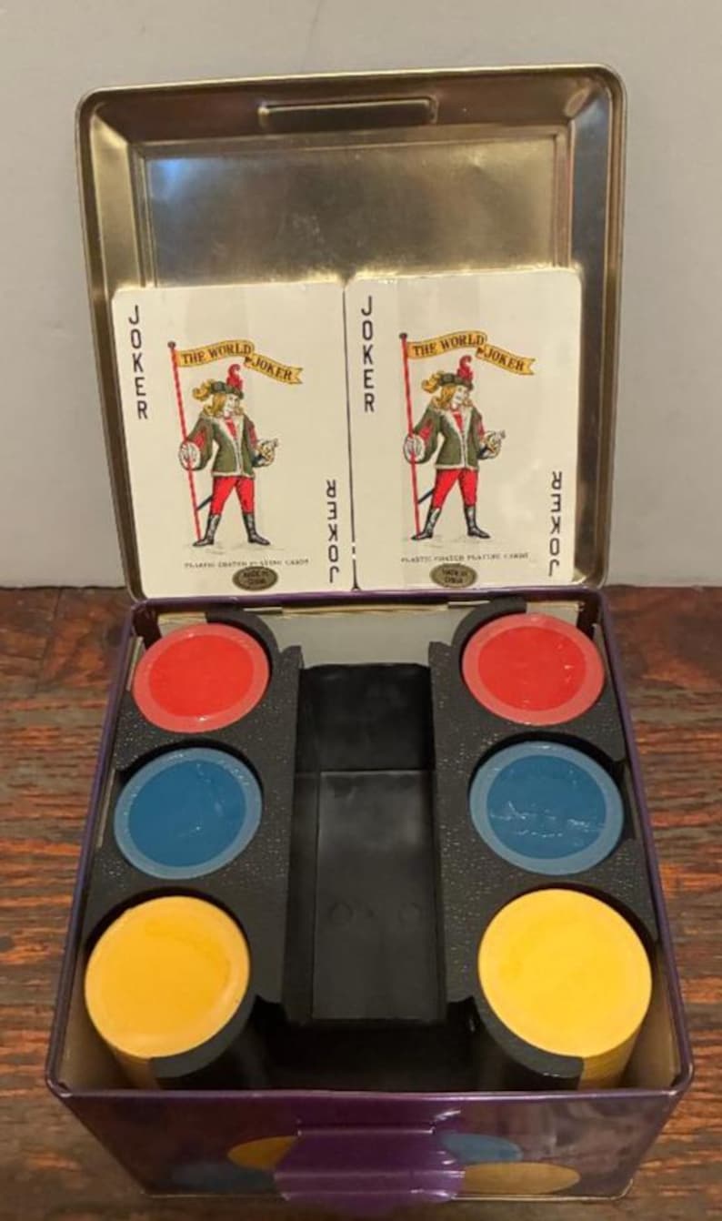 May include: A vintage card game set in a metal tin. The set includes two "Joker" playing cards and colorful poker chips in red, blue, and yellow. The tin is purple with a silver lid.
