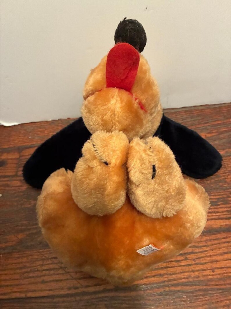May include: A plush toy dog with a black head and wings, tan body, and red accents. The dog is lying on its back, with its paws and belly visible. The toy has a soft, fuzzy texture.