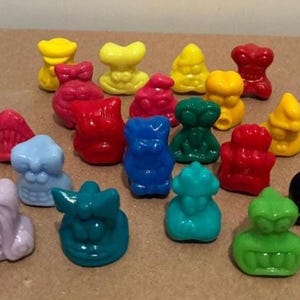 以下が含まれることがあります： 黄色、赤、青、緑、黒など、さまざまな形と色をした、小さくてカラフルなプラスチック製のフィギュアのコレクション。 フィギュアは光沢のある仕上げで、茶色の表面に配置されています。