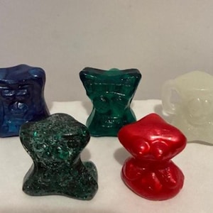 May include: Five colorful, abstract glass sculptures in shades of blue, green, red, and white. The shapes are organic and textured, with a glossy finish. The sculptures are arranged on a white surface.