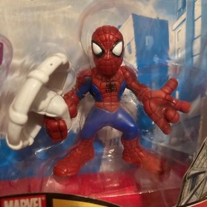May include: A Spider-Man action figure in a clear plastic package. The figure is red, blue, and white, with a web design on the suit. The figure is holding a white web shooter. The package has the Marvel logo.