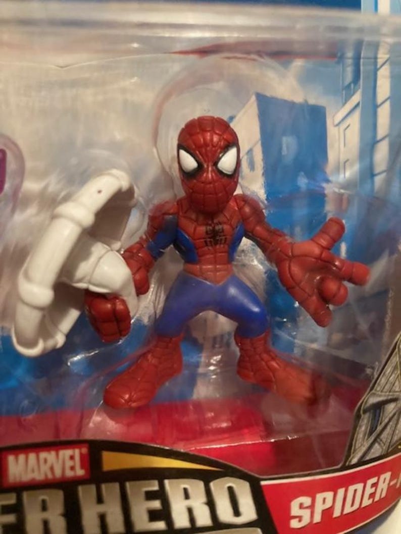 May include: A Spider-Man action figure in a clear plastic package. The figure is red, blue, and white, with a web design on the suit. The figure is holding a white web shooter. The package has the Marvel logo.