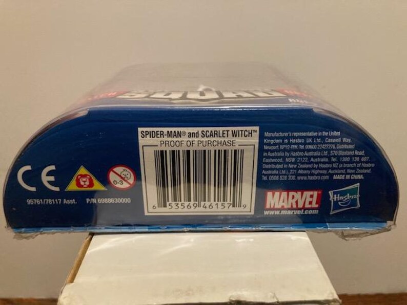 May include: A blue and red action figure package featuring the text "SPIDER-MAN and SCARLET WITCH". The package includes a barcode, the Marvel logo, and the Hasbro logo. The age range is 0-3.