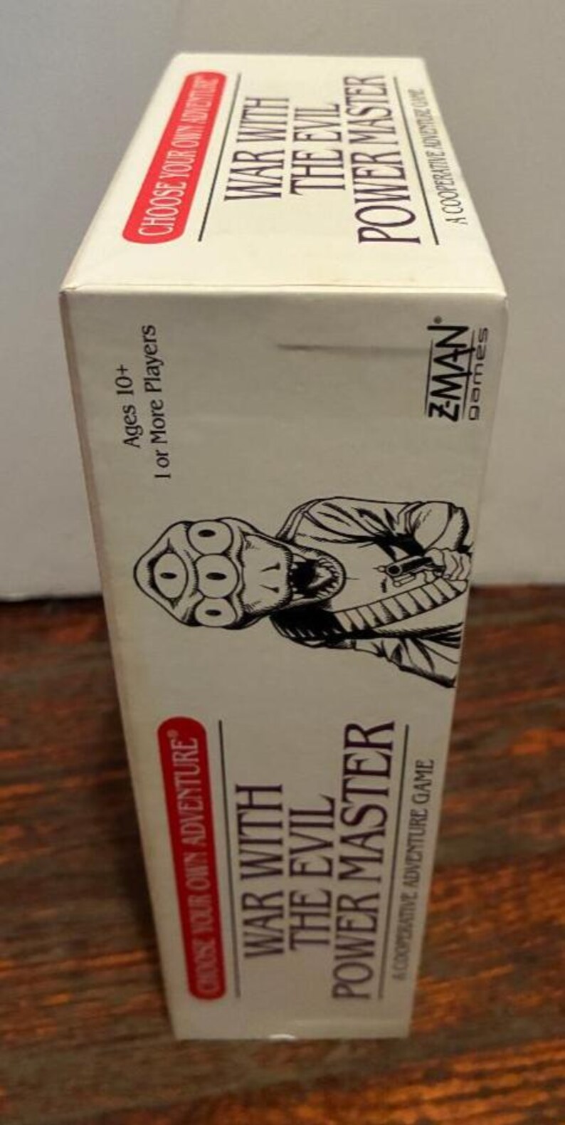 K&ouml;nnte beinhalten: Ein Brettspielkarton mit dem Titel "War With The Evil Power Master". Die Schachtel zeigt eine Schwarz-Wei&szlig;-Illustration einer Kreatur mit mehreren Augen. Der Text "Choose Your Own Adventure" ist ebenfalls sichtbar.