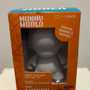 May include: A gray mini Munny vinyl art toy inside an orange and blue box. The box reads "Munny World" and "Create Your Own Vinyl Art Toy!" Includes 3 wipe-off markers. The box also says "Design, Admire & Inspire!"