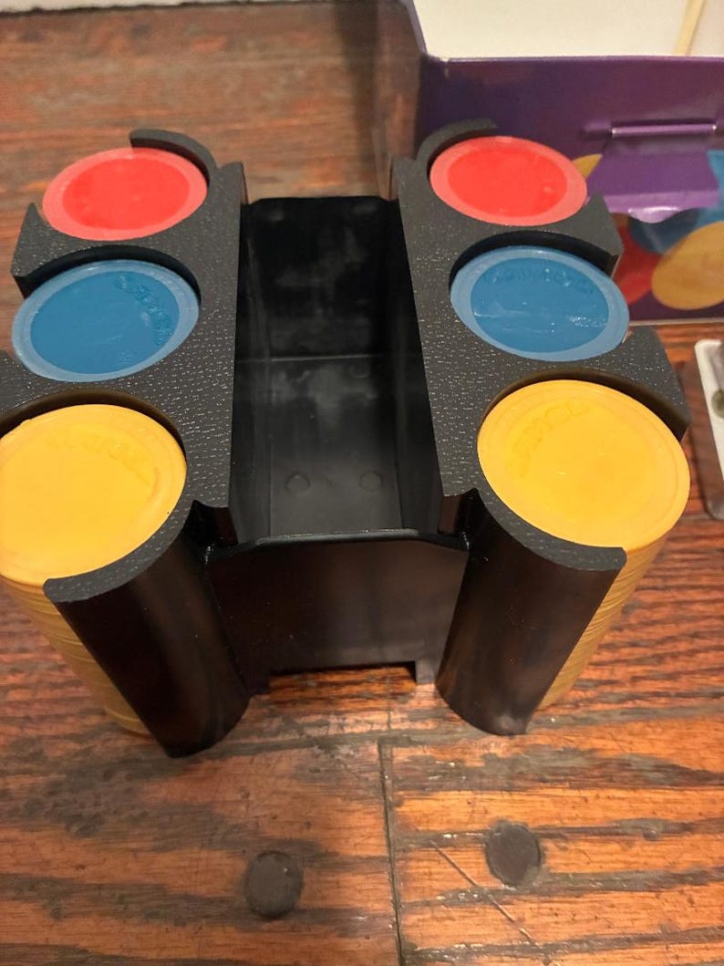 May include: A black plastic game chip holder with stacks of yellow, red, and blue chips. The holder has three slots, each holding a stack of chips. The chips are round and have the word "SPADES" printed on them.