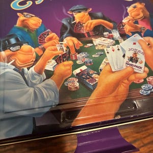 May include: A vintage Camel cigarette tin featuring a poker game scene with anthropomorphic camels. The tin is primarily purple with the word "CAMEL" in large, yellow letters. The poker scene includes playing cards, chips, and the text "JOKER HARD PACK".