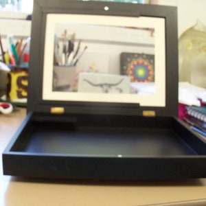 May include: A black wooden box with a hinged lid and a black velvet interior. The lid is open and the interior is empty.