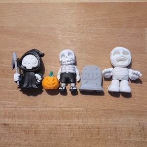 Könnte beinhalten: Ein Set aus vier Halloween-Figuren, darunter ein schwarz gekleideter Sensenmann mit einer Sense, ein Skelett in einem schwarzen Badeanzug, ein kleiner Kürbis und eine weiße Mumie mit einem Grabstein, auf dem "RIP" steht.