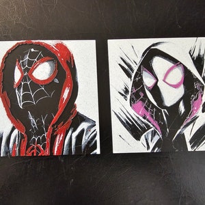 May include: Two black and white illustrations of masked figures wearing red and pink hooded sweatshirts. The figures are drawn in a stylised, graphic style.