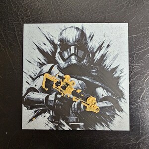 May include: A black and white illustration of a Stormtrooper from Star Wars holding a blaster rifle. The blaster rifle has gold accents.