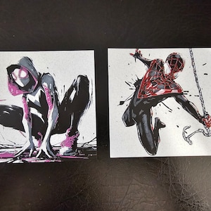 May include: Two illustrations of Spider-Man characters. The first illustration is of Spider-Gwen, a female Spider-Man character with a black and white suit and pink accents. The second illustration is of Miles Morales, a male Spider-Man character with a black and red suit.