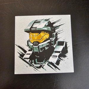 Puede incluir: Una ilustración en negro y verde de Master Chief, un personaje de la serie de videojuegos Halo, que lleva un casco con una visera amarilla. La ilustración está sobre un fondo blanco.