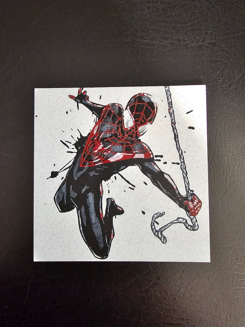 May include: A black and red stylised illustration of Spider-Man swinging through the air with a web line. The background is white with black splatters of paint.