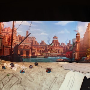 May include: A multi-panel game screen featuring a detailed illustration of a fantasy city by a body of water. Dice, a map, and other gaming accessories are in the foreground. The city has red-orange buildings and a blue sky.