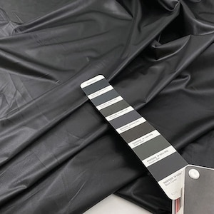 May include: A black leather fabric swatch with a Pantone color chart. The chart shows different shades of black and gray. The text on the chart includes "Pantone" and "Black Onyx".