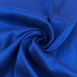 May include: A close-up shot of a vibrant, royal blue fabric with a silky sheen. The fabric is draped and folded, creating soft curves and shadows. The material appears smooth and luxurious, with a slight sheen that reflects light.