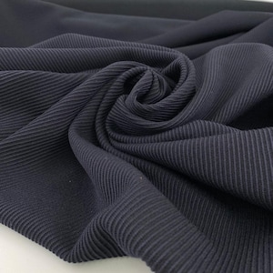 Könnte beinhalten: Nahaufnahme eines dunkelblauen Stoffes mit Rippenstruktur. Der Stoff ist gefaltet und drapiert, wodurch die Richtung des Rippenmusters hervorgehoben wird. Das Material wirkt weich und flexibel, geeignet für Kleidung oder Heimdekoration.
