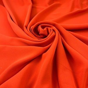 May include: Close-up of vibrant orange fabric, artfully draped and swirled. The material has a soft, velvety texture, with folds and shadows creating depth. The color is a rich, saturated hue, suitable for apparel or home decor.