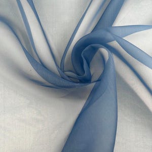 May include: A sheer, lightweight fabric in a soft shade of dusty blue. The material is arranged in a swirling, gathered pattern, creating overlapping layers that transition from deep blue tones to lighter, translucent white areas throughout.