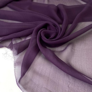 May include: Close-up of a flowing, sheer fabric in a deep purple hue. The fabric is draped and swirled, creating soft folds and a textured appearance. The edges of the fabric have a frayed detail.