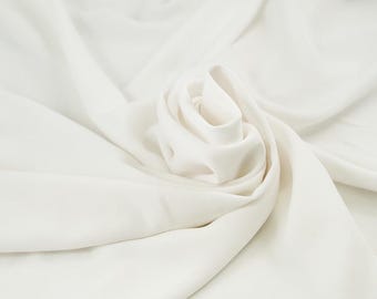 Puede incluir: Primer plano de una tela blanca con pliegues suaves y una disposición en forma de rosa en el centro. La tela tiene una textura suave y un acabado mate, creando una apariencia delicada y elegante. El efecto general es de movimiento suave y sutil juego de luces.