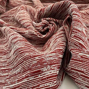 Op de afbeelding: Close-up van een textiel met een herhalend patroon van witte lijnen op een dieprode achtergrond. De stof is gevouwen en gedrapeerd, wat de textuur en het ontwerp laat zien. Dit textiel kan worden gebruikt voor bekleding of kleding.